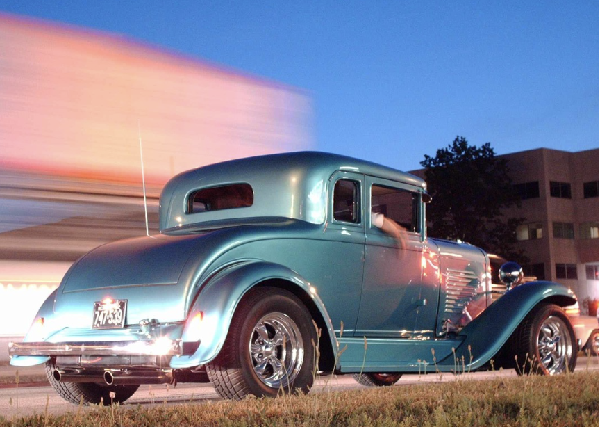 A classic teal hot rod cruising down the street at dusk